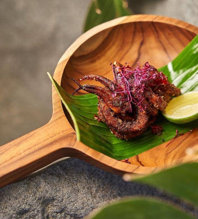 A wooden plate with seafood and garnished with lime and edible flowers, served in Ubud Restaurant