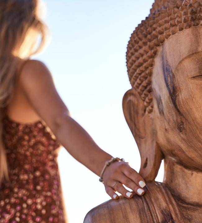 The blur picture of a woman touching a wooden Buddha statue in UBUD hotel terrace