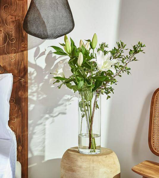 The bedside table in the UBUD family suite decorated with glass vase with white lilies